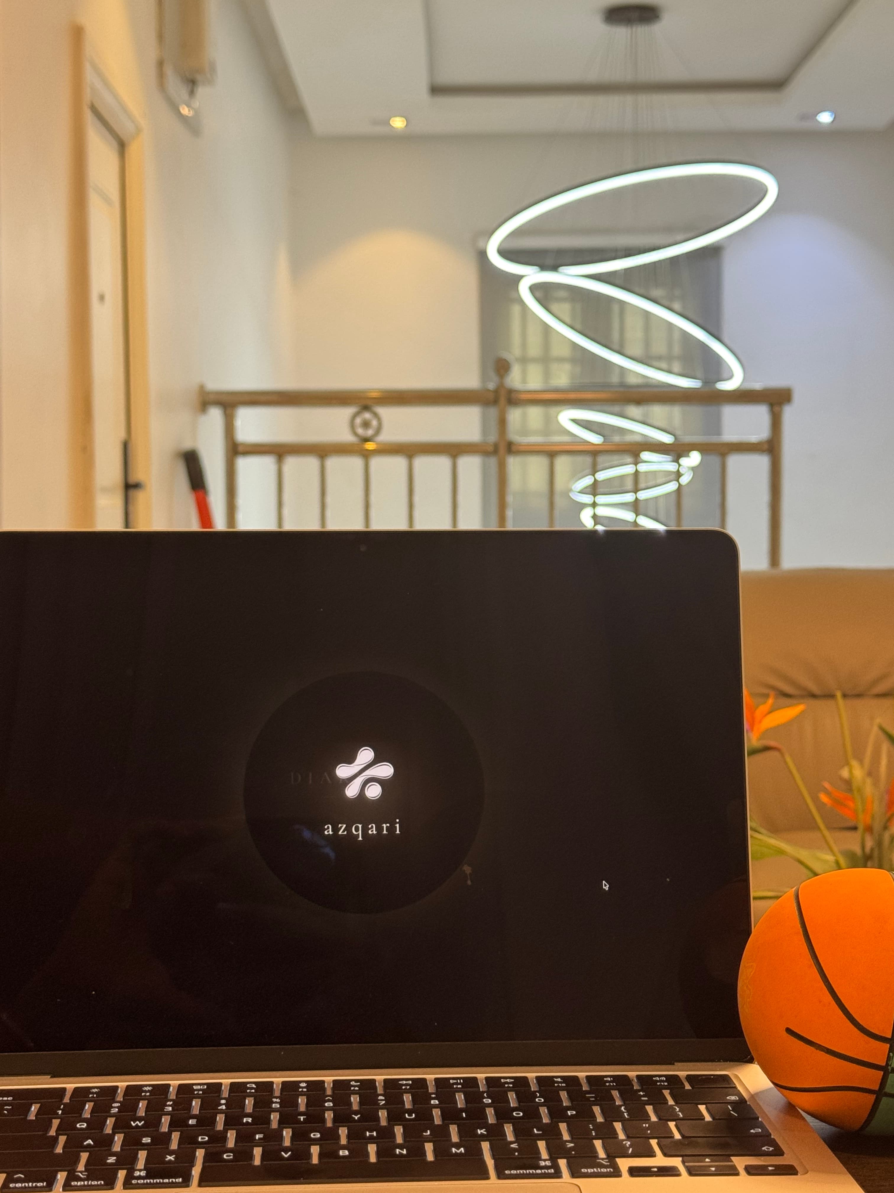 An Azqari-equipped space — a laptop displaying the Azqari logo beneath a sculptural lighting installation.